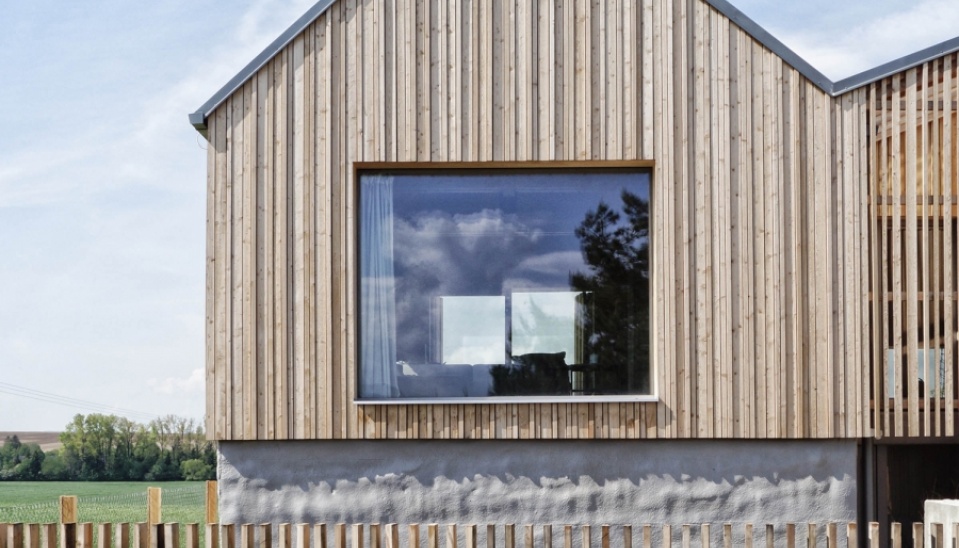 Detail – drevená reliéfna fasáda s veľkým bezrámovým oknom a železobetónová podstava s nepravidelným povrchom pripomínajúca steny starých sýpok a humien, foto: archív autorov